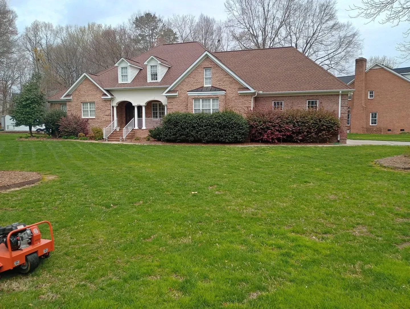 Core aeration in progress on the lawn outside a brick home.