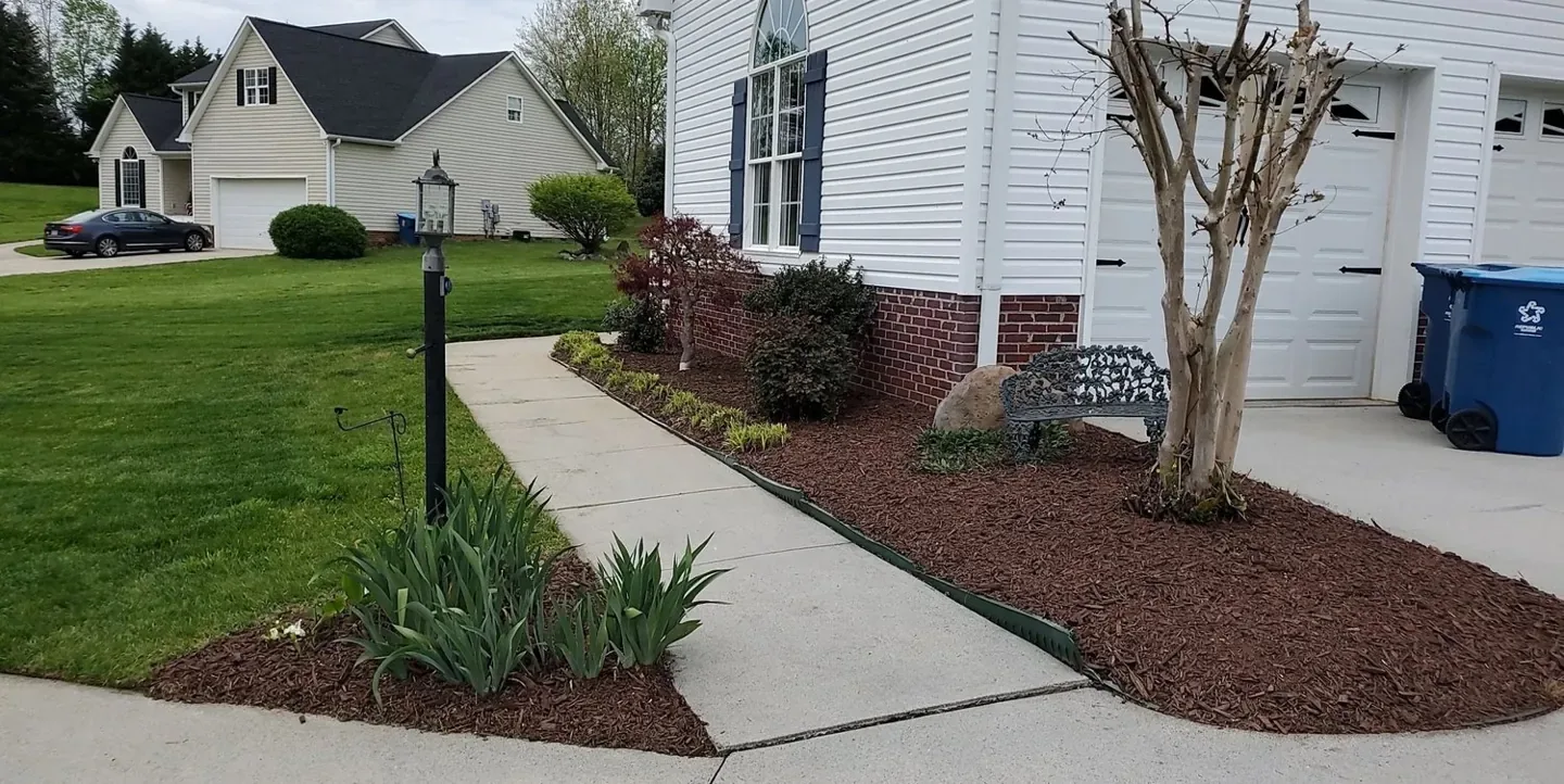 Fresh brown mulch around shrubs and plants in a front garden bed.
