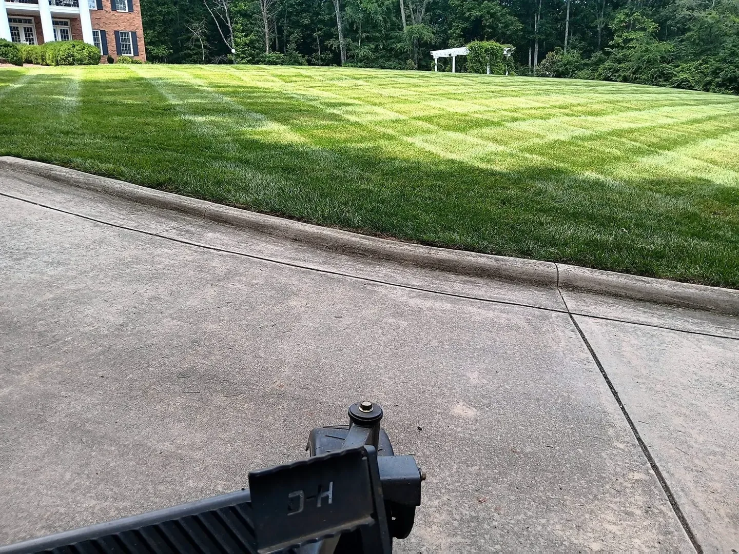 Neat lawn stripes along the edge of a concrete driveway.
