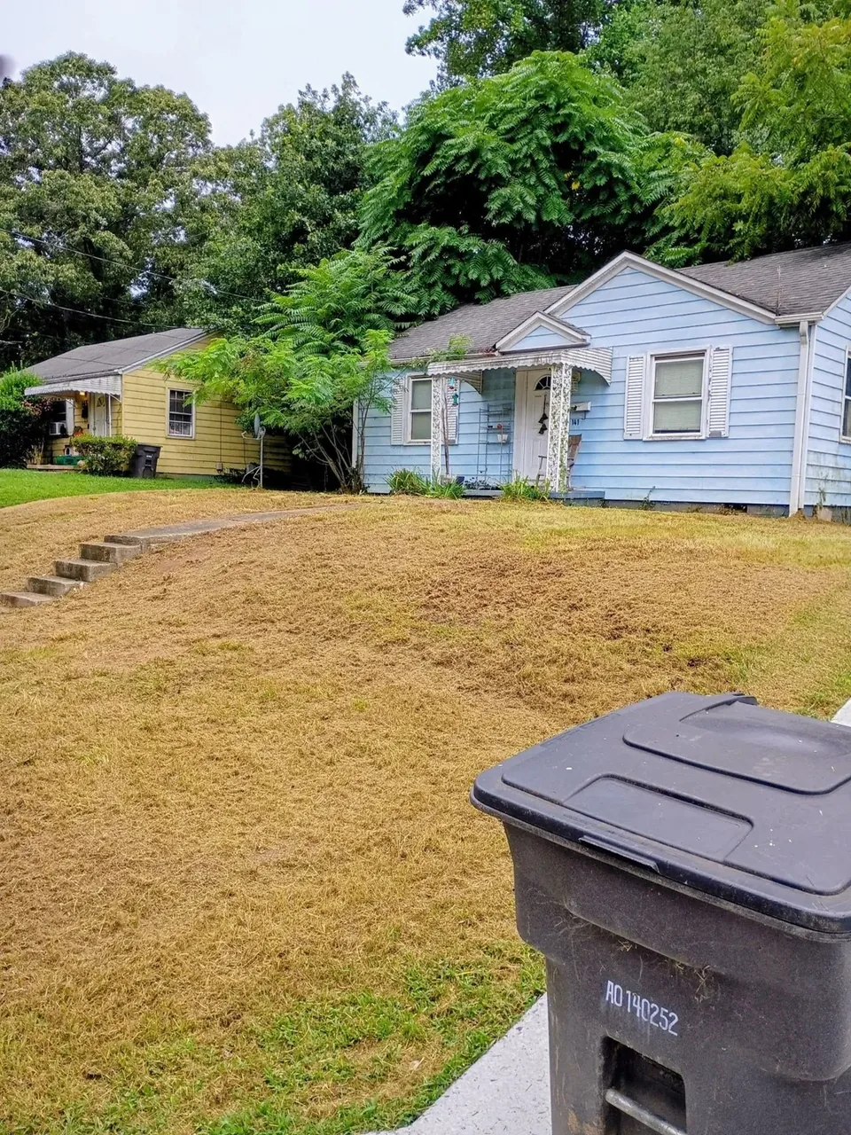 Mowed hillside and cleared lawn around a small blue house after cleanup.