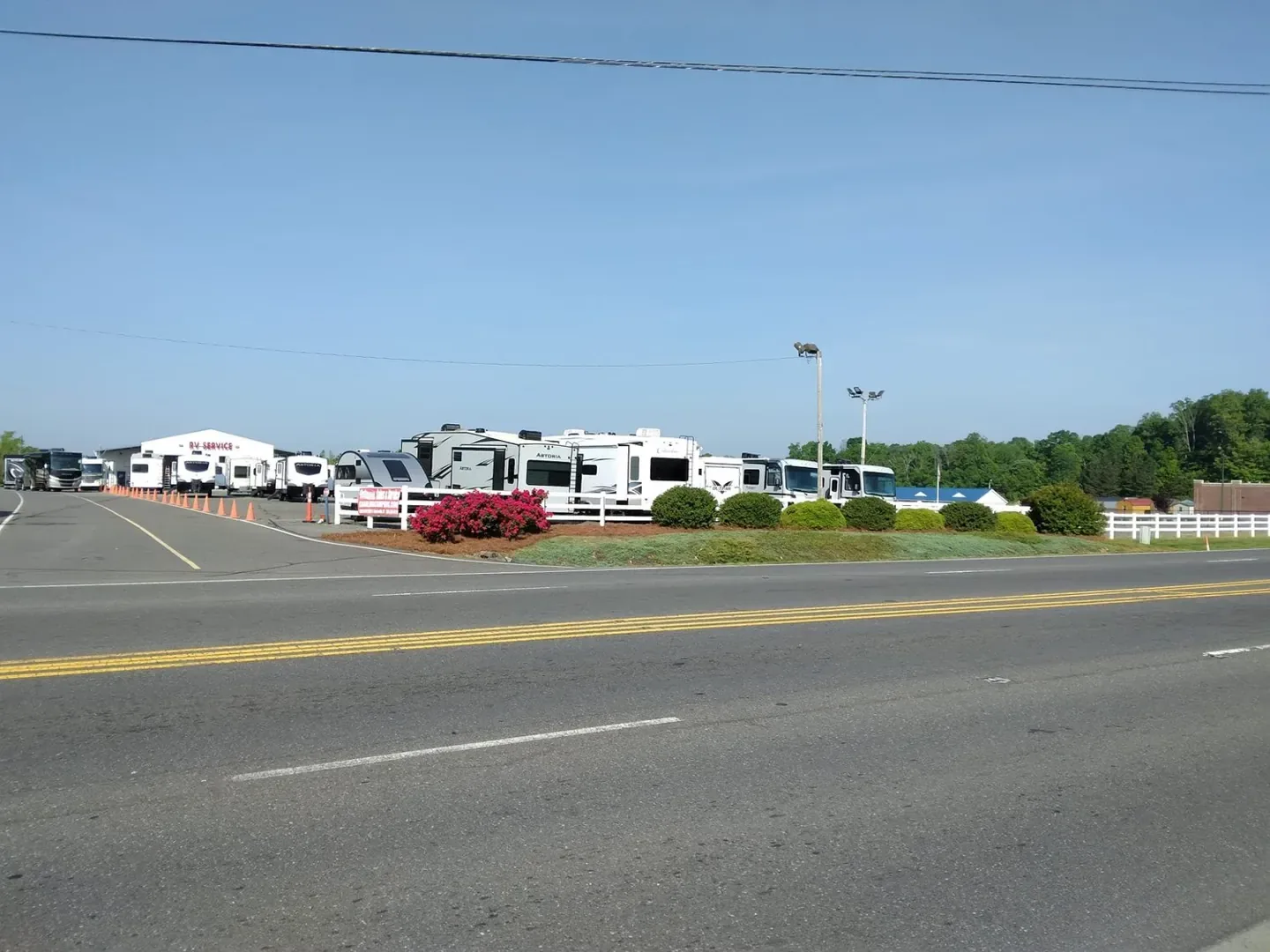 Roadside view of fresh pine needles and trimmed beds at an RV sales lot.