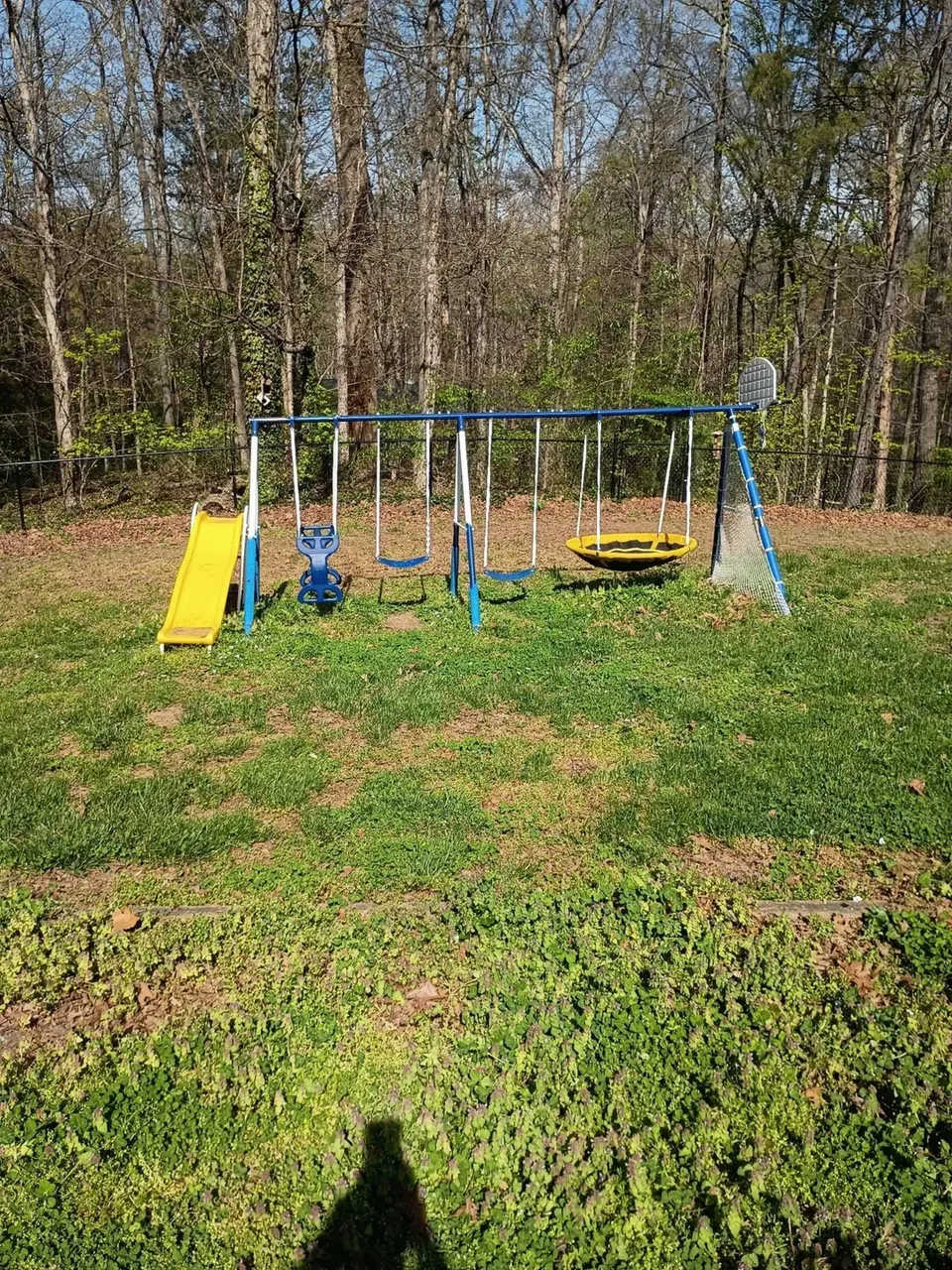 Grass and weeds around a backyard playset before bed installation.