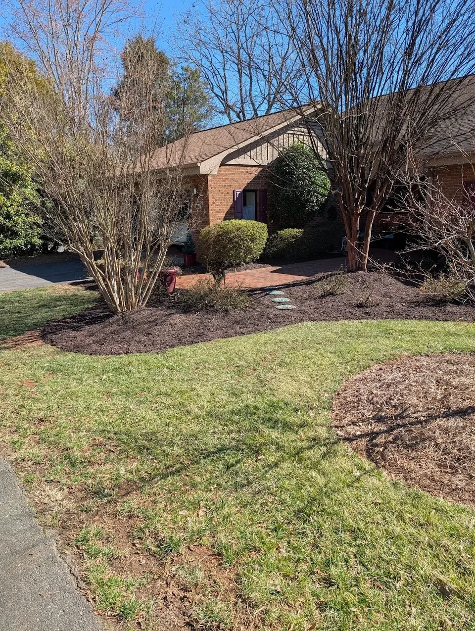 Fresh mulch and cleaned planting beds beside a brick walkway.