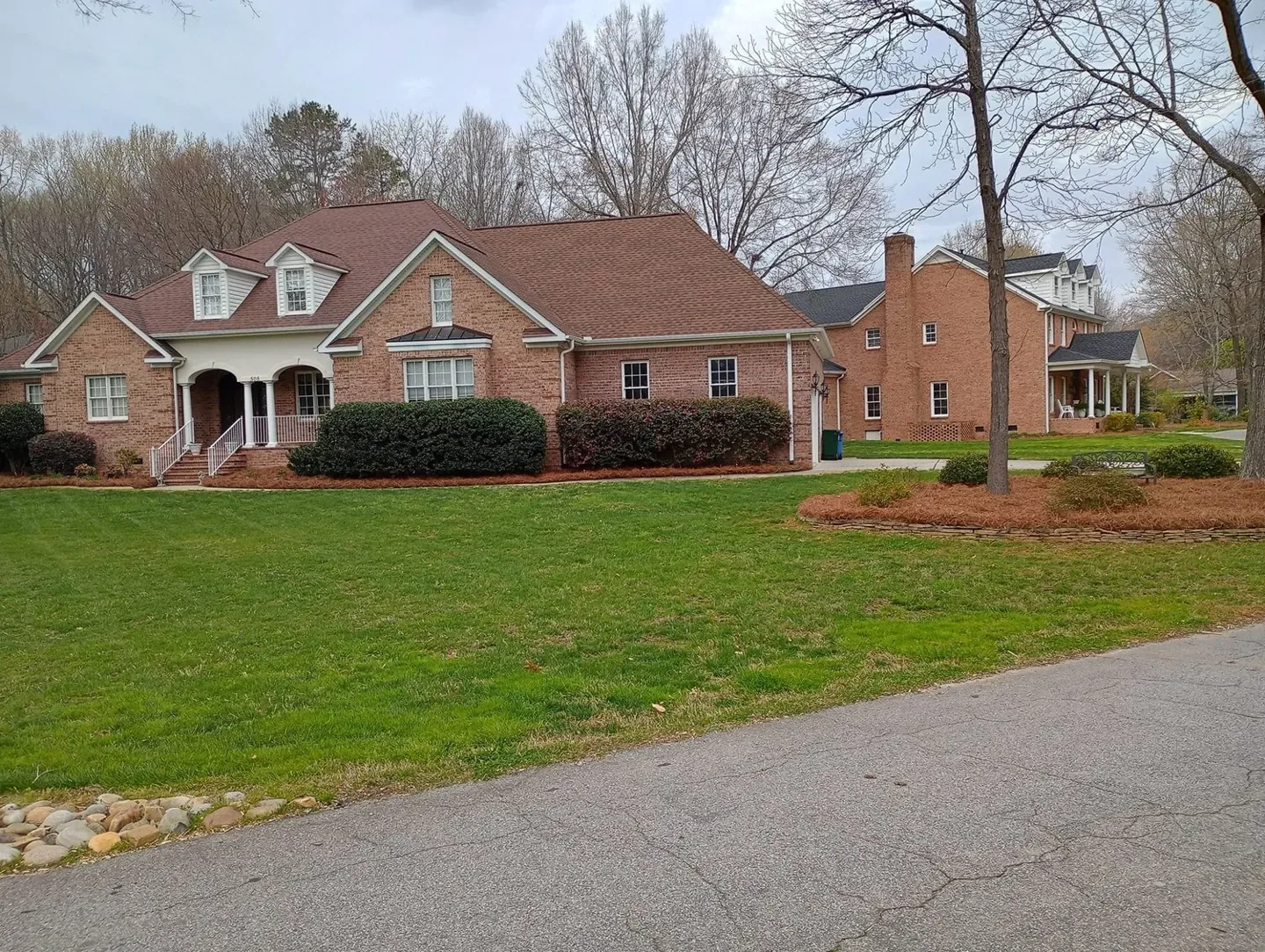 Brick home with a freshly maintained lawn and pine needle beds.
