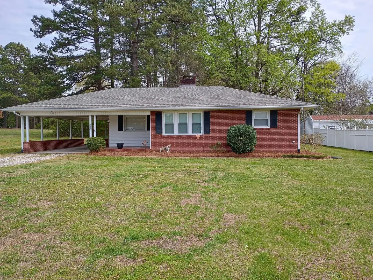 Pruned shrubs and refreshed pine needle beds at a brick home.